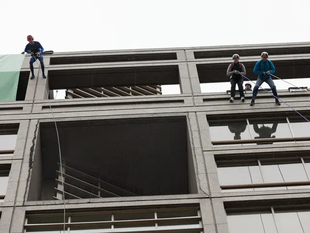 In this image I can see a building and few people on wall with rope. I can see all are wearing...