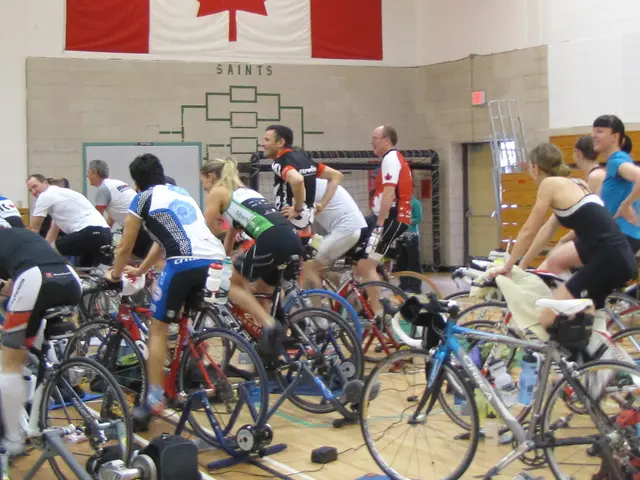 In this image we can see a group of people sitting on bicycles placed on stands, we can also see...